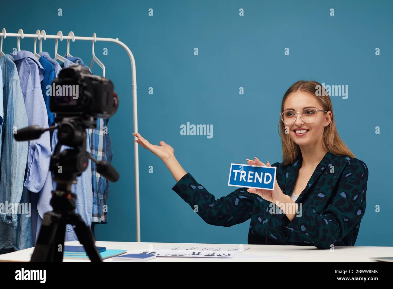 Beauté blogueur assis à la table et pointant sur les vêtements elle parlant avec des disciples au sujet de la mode en ligne Banque D'Images