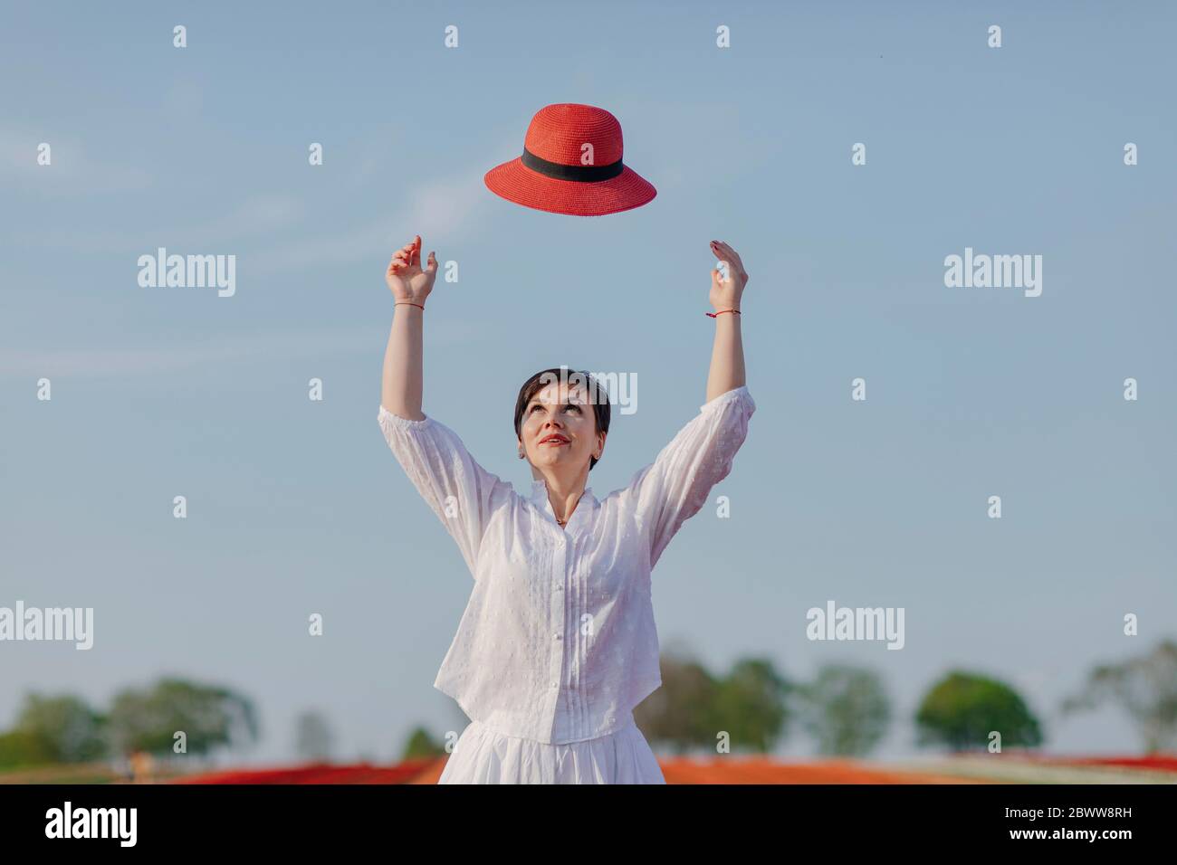 Portrait d'une femme qui jette un chapeau rouge dans l'air Banque D'Images