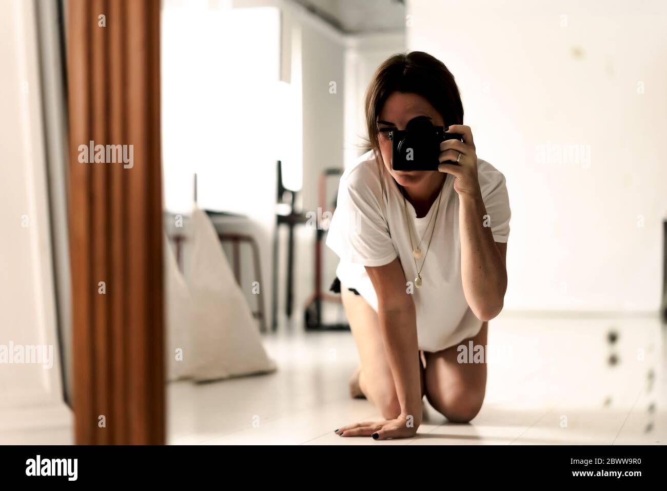 Image miroir d'une femme mûre agenouillée sur le sol en prenant des photos avec l'appareil photo Banque D'Images