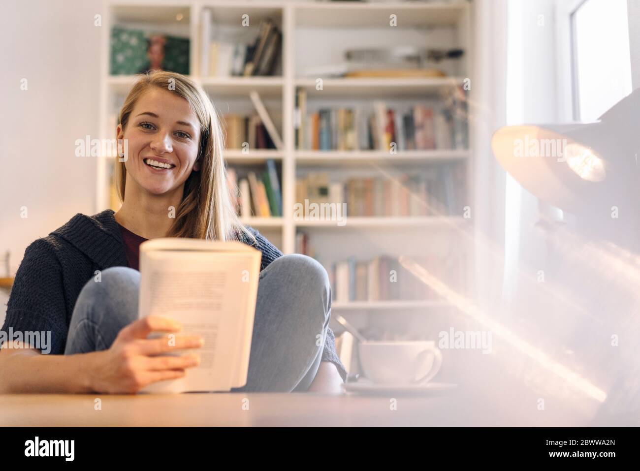 Portrait d'une jeune femme heureuse lisant un livre à la maison Banque D'Images