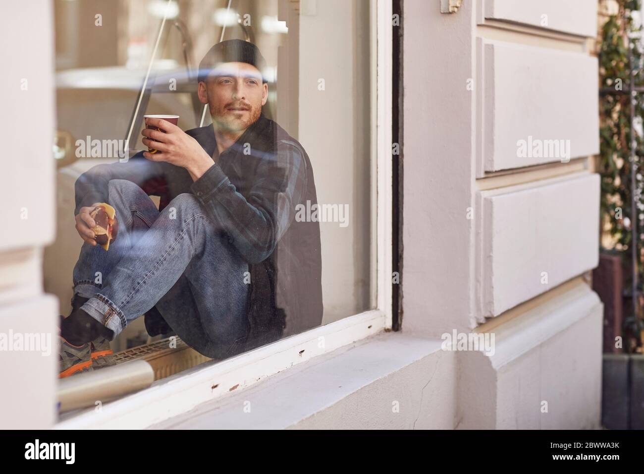 Homme en train de rénover l'emplacement de l'atelier, assis sur le rebord de la fenêtre, en buvant du café Banque D'Images