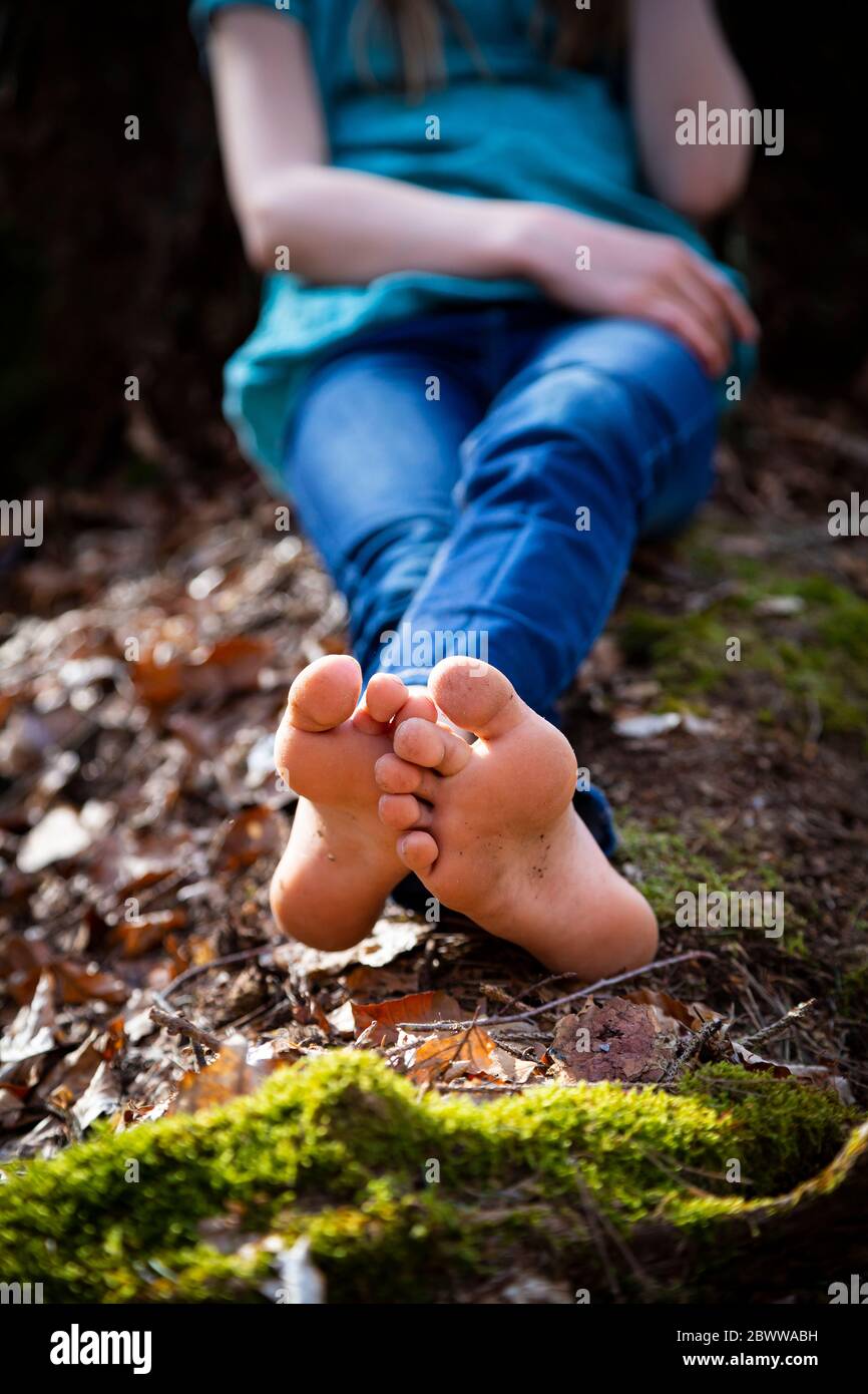 Vue rognée d'une fille assise pieds nus sur le sol en forêt Banque D'Images