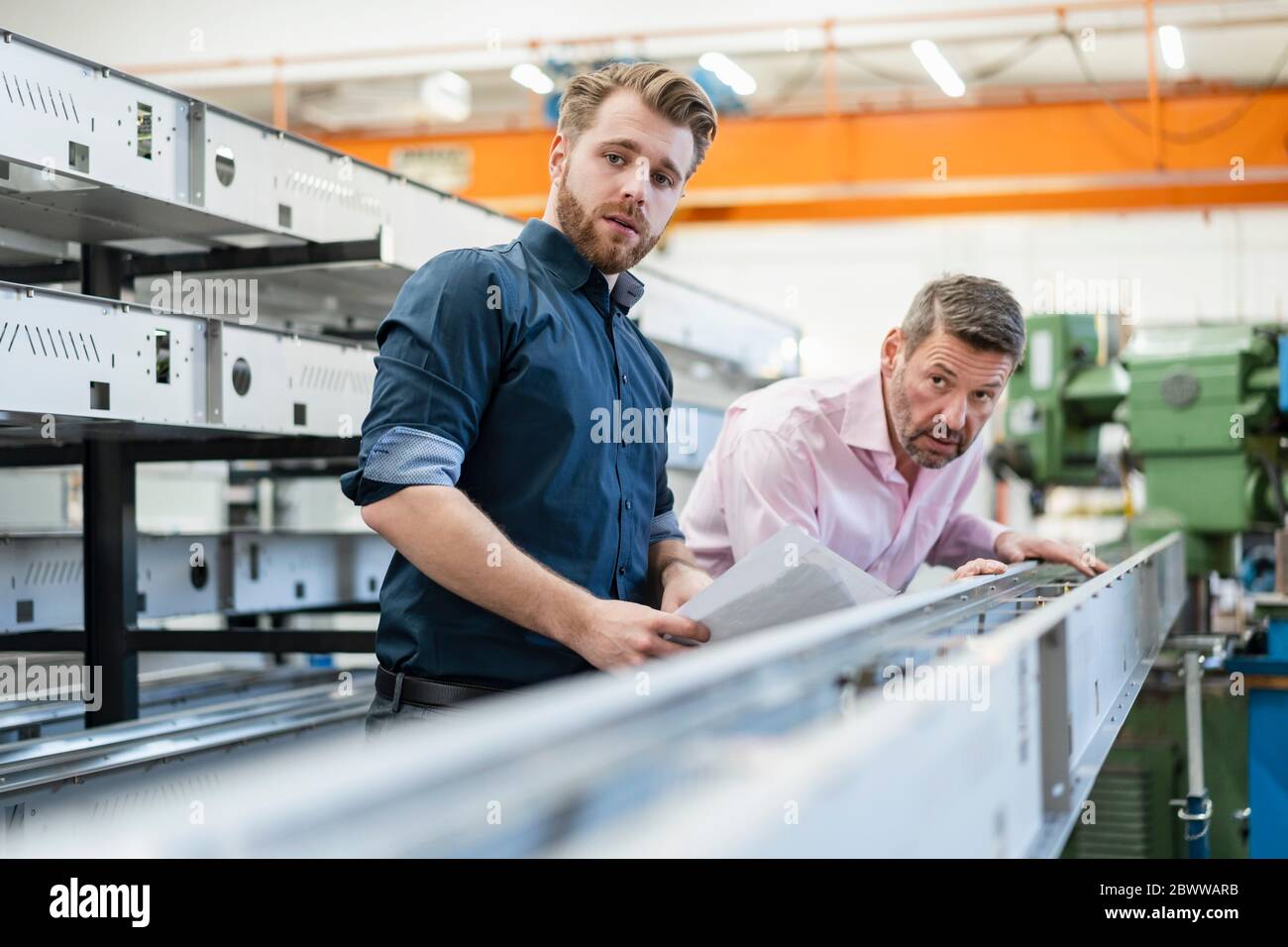 Deux hommes examinant un morceau de métal dans une usine Banque D'Images