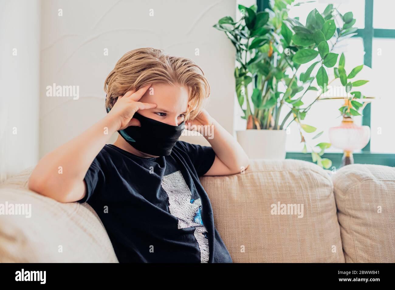 Garçon assis sur un canapé dans la salle de séjour à la maison portant un masque Banque D'Images