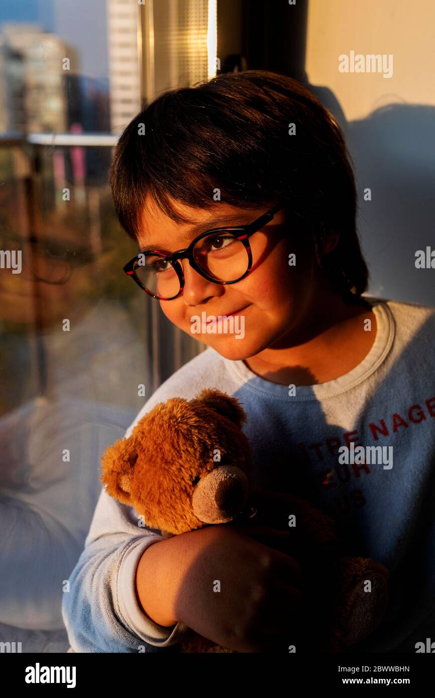 Portrait d'un garçon souriant avec un ours en peluche, en regardant par la fenêtre le soir Banque D'Images