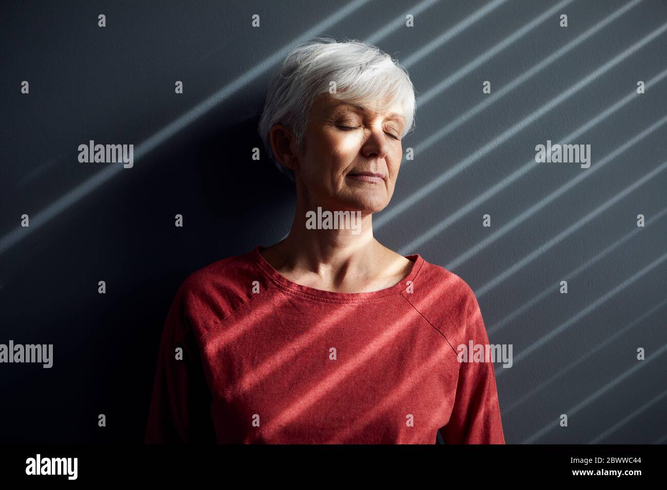 Portrait d'une femme âgée avec les yeux fermés, penchée contre le mur Banque D'Images