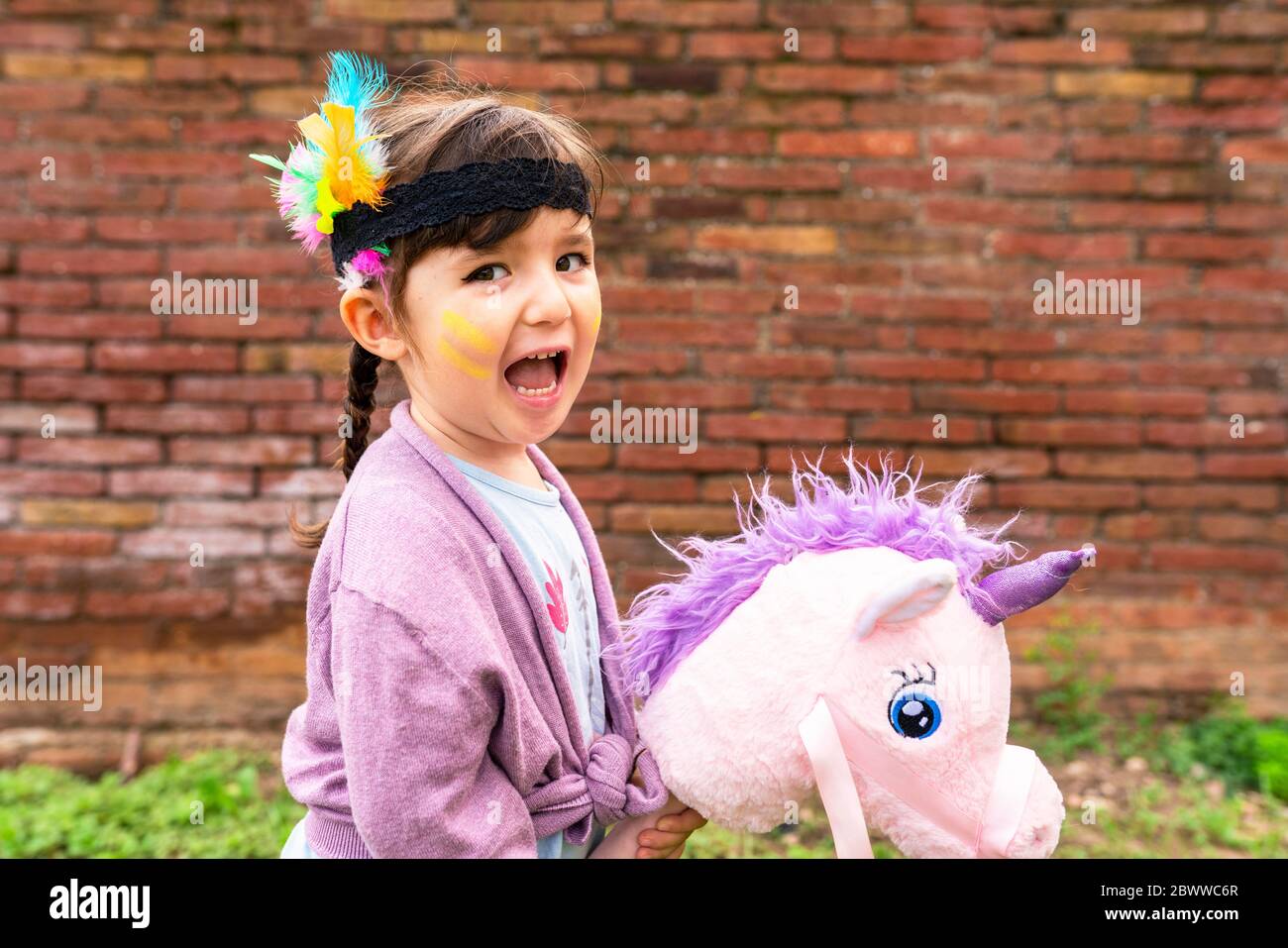 Portrait d'une fille avec des tresses et une plume de headaddress à cheval d'une licorne rose Banque D'Images