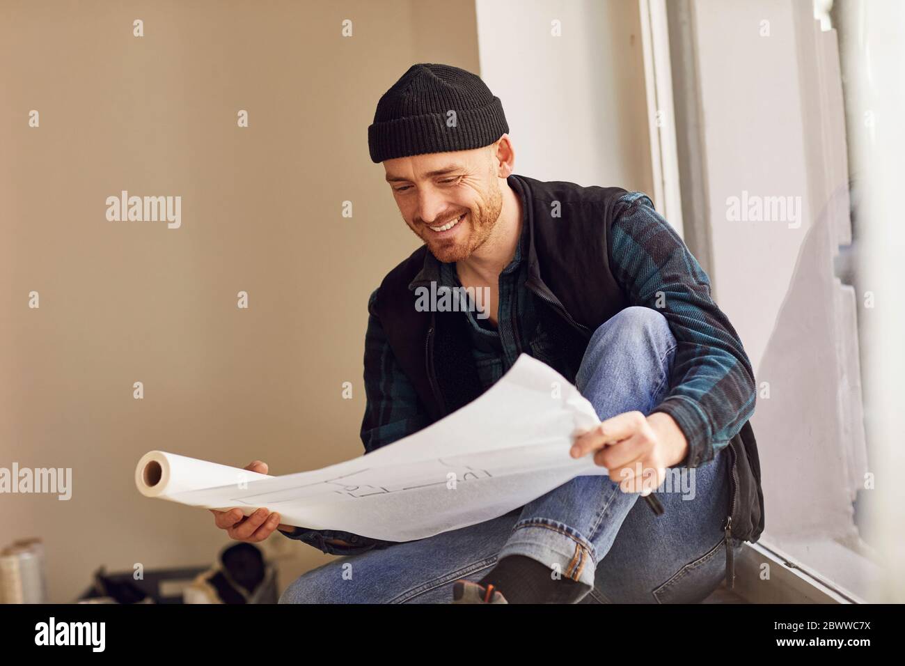Homme en train de rénover l'atelier, assis sur le rebord de la fenêtre, étudiant le plan Banque D'Images