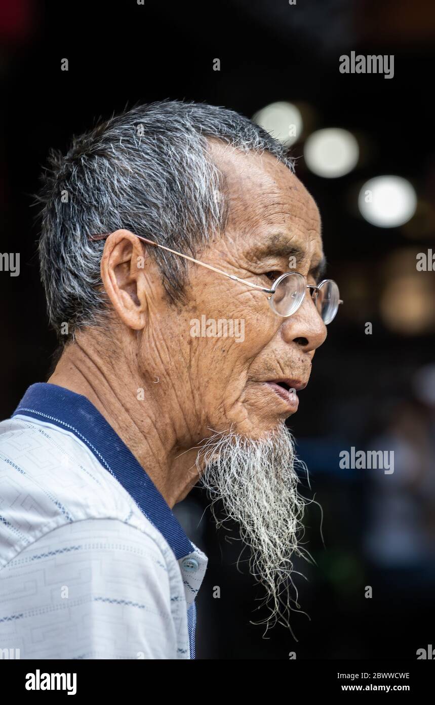 Feng Huang, Chine - août 2019 : Portrait d'un vieil homme chinois avec une barbe grise et de petites lunettes rondes Banque D'Images