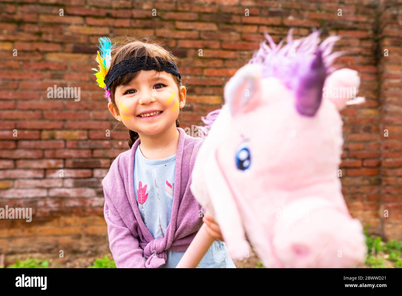 Portrait d'une fille avec des tresses et une plume de headaddress à cheval d'une licorne rose Banque D'Images