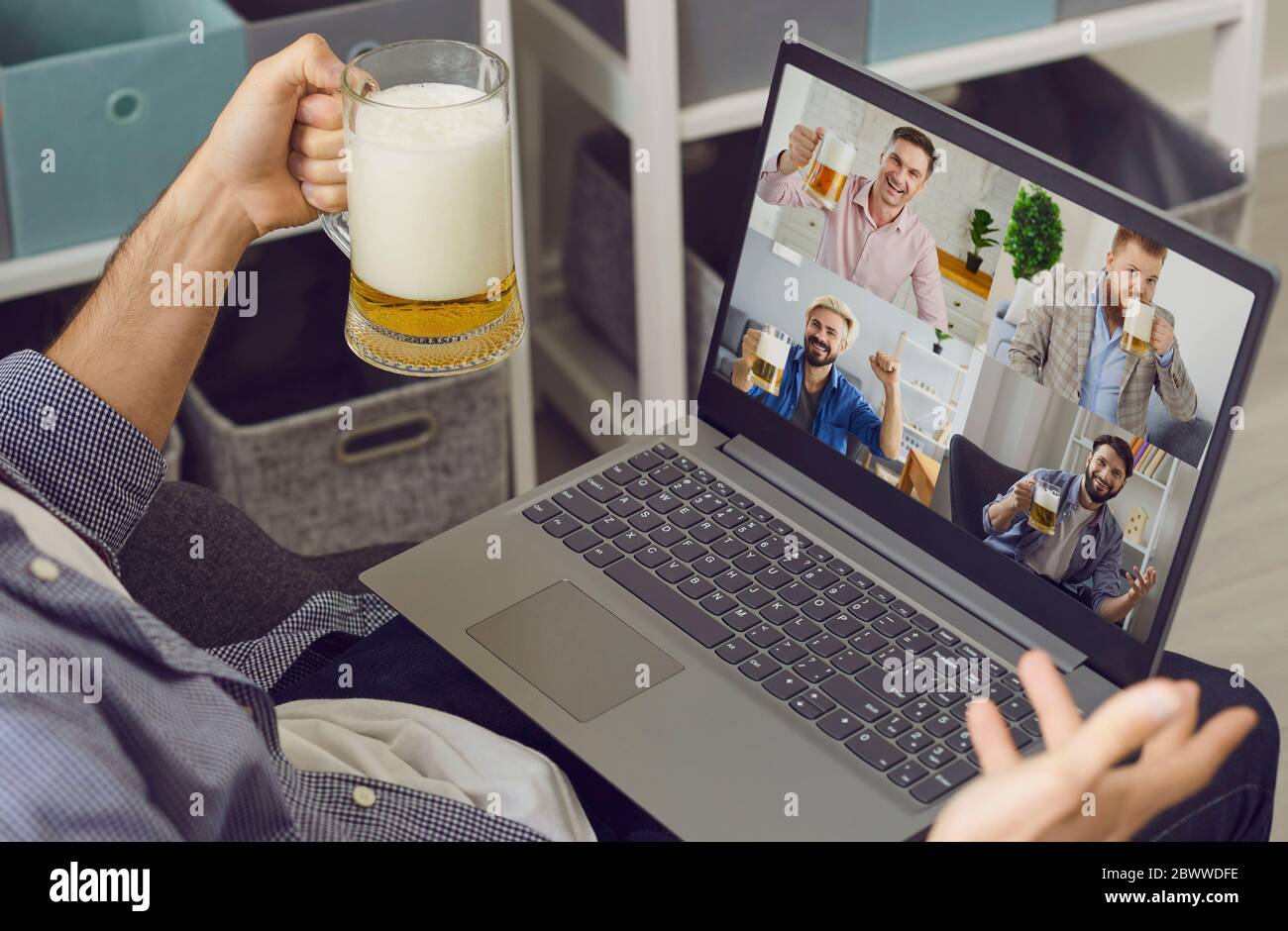 Chat vidéo en ligne avec vos amis. Un homme avec un verre de bière accueille des amis qui ont un ordinateur portable de vidéo conférence à la maison. Banque D'Images