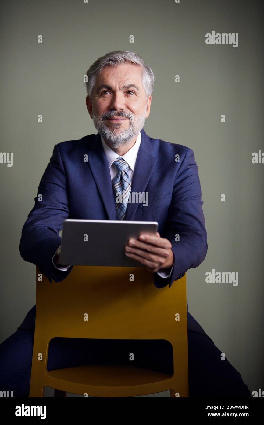 Portrait d'un homme d'affaires mature assis sur une chaise à l'aide d'une tablette Banque D'Images