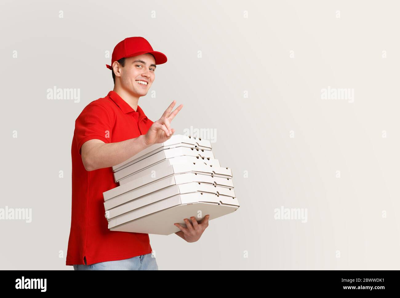 Beaucoup de pizza à la maison. Un coursier souriant affiche le signe de paix et contient de nombreuses boîtes Banque D'Images