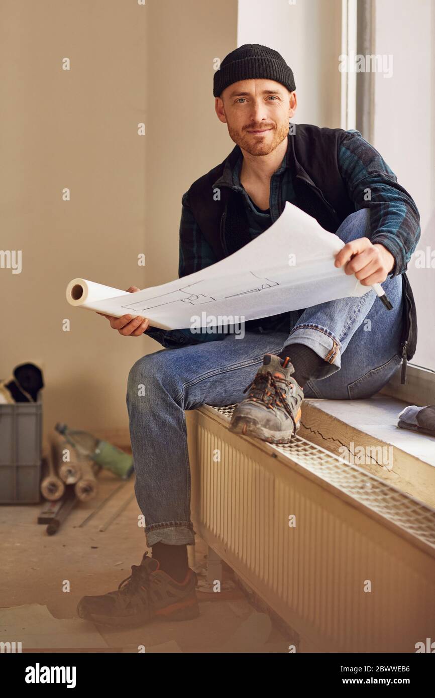Homme en train de rénover l'atelier, assis sur le rebord de la fenêtre, étudiant le plan Banque D'Images