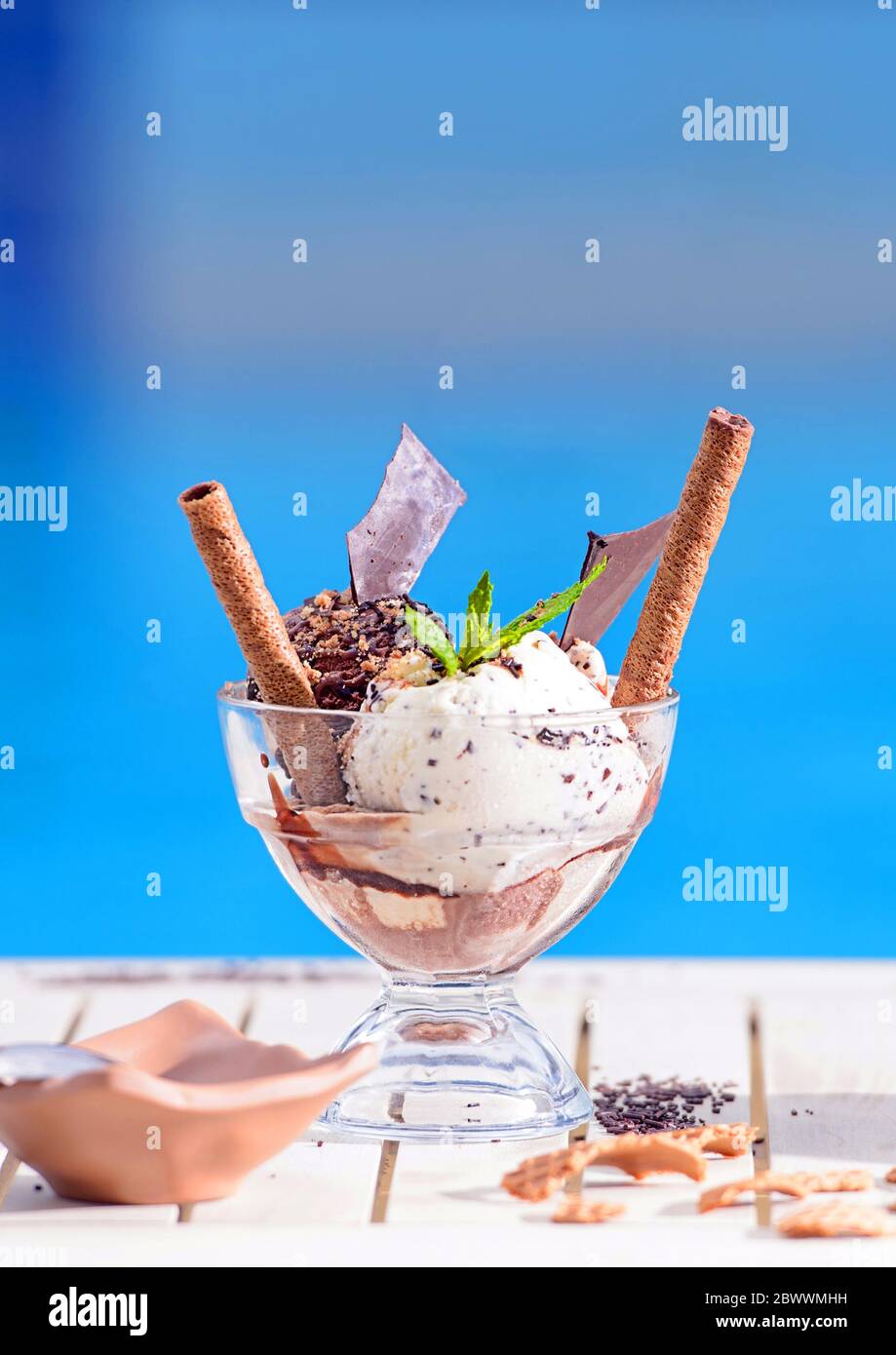 Gros plan d'un bol en verre avec des boules de glace à la menthe et à la vanille sur fond bokeh flou avec espace de copie. Rouleaux de chocolat gaufré sur table blanche bleue Banque D'Images