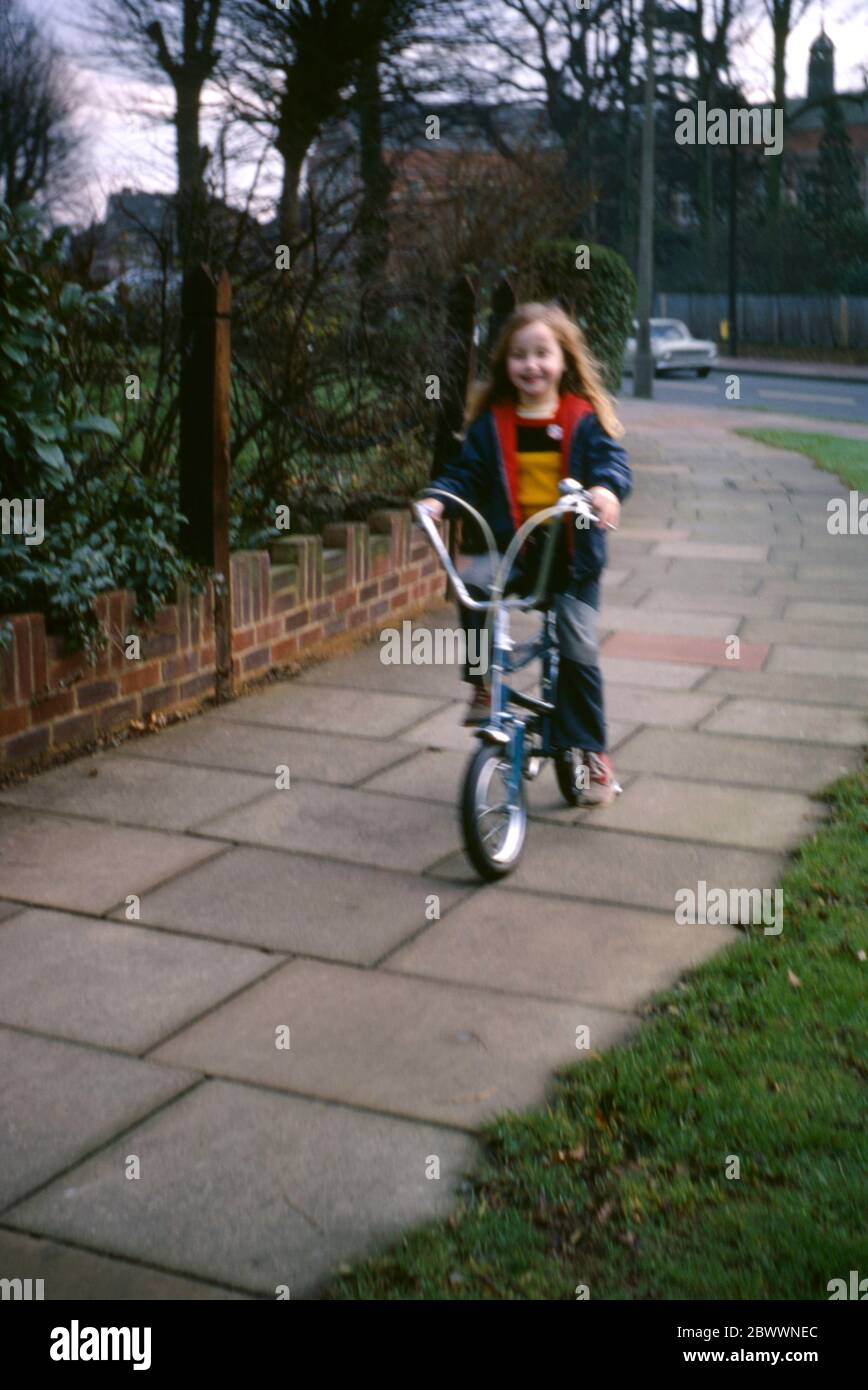 Une fille de 7 ans portant un Jean menuisier et une veste bleue, à bord de  son vélo Raleigh Tomahawk le long du pavé dans la banlieue de Londres,  Hatch End, Middlesex,