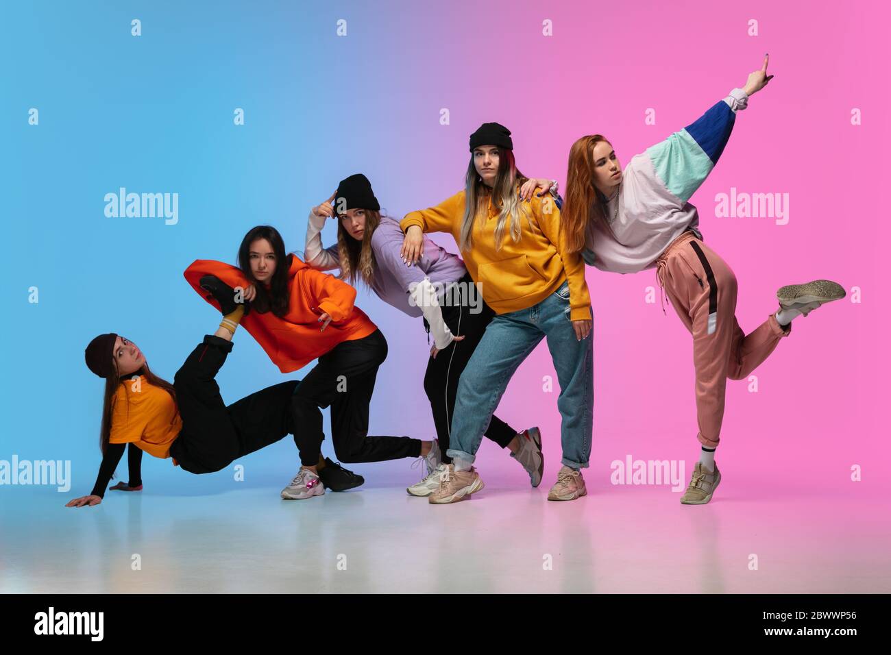 Groupe de danseurs, garçons et filles dansant hip-hop dans des vêtements  élégants sur fond de dégradé coloré à la salle de danse au néon. Culture,  mouvement, style et mode de jeunesse, action.