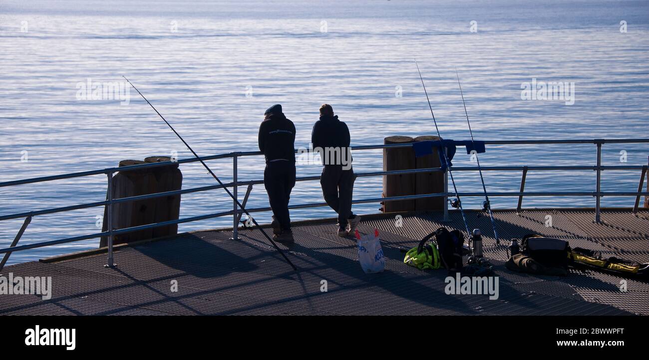 Deux hommes silhouetés pêchant au bout d'un quai et regardant la mer. Banque D'Images