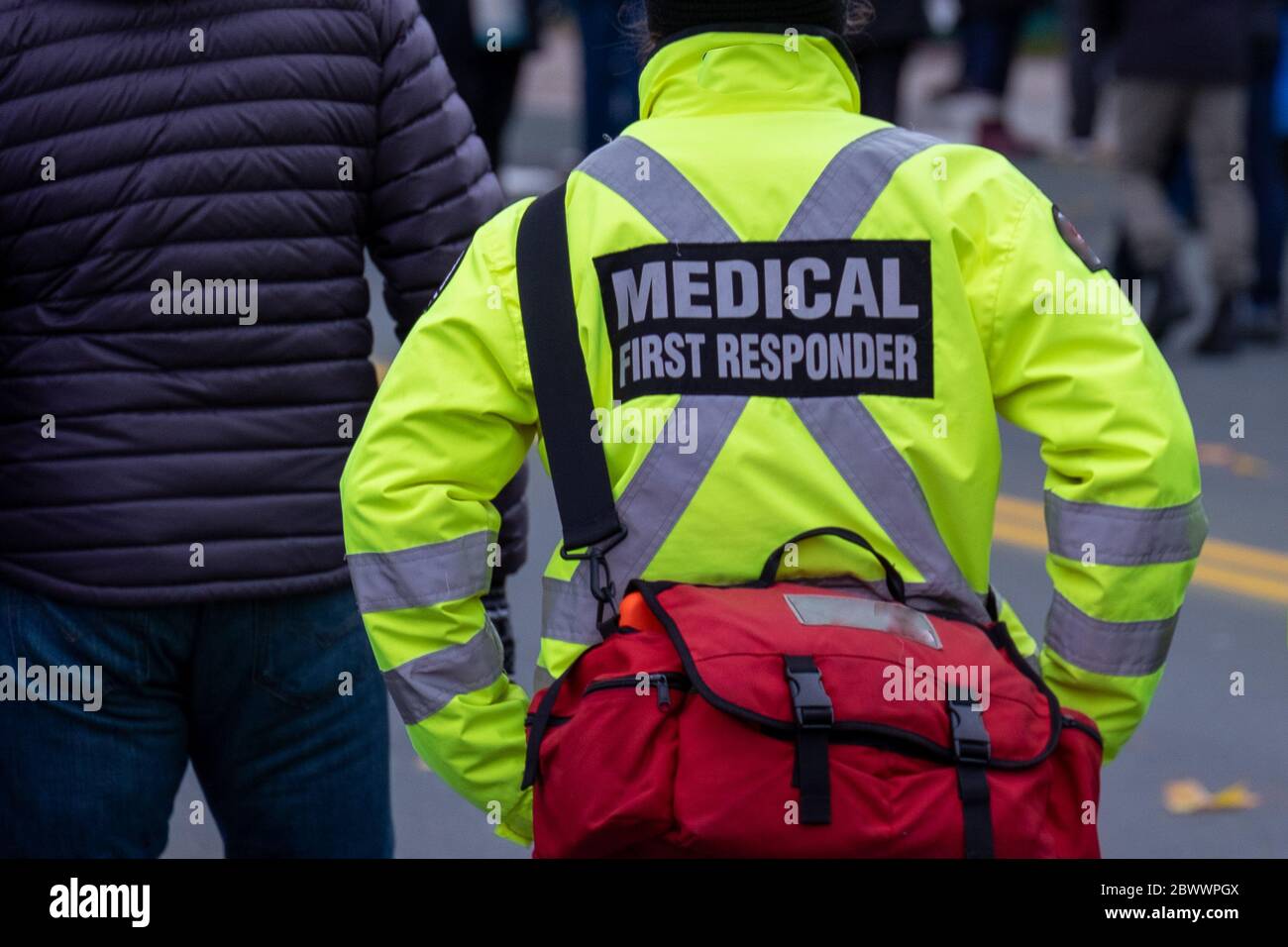 Un uniforme de secouriste médical jaune vif porté par un grand homme dans une rue bondée.le manteau a une croix grise réfléchissante à travers le dos. Banque D'Images