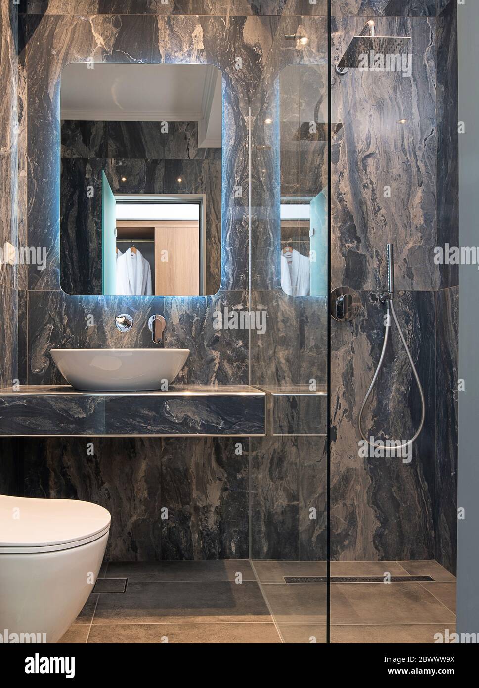 Vue sur la façade de la salle de bains contemporaine en marbre gris avec lavabo, miroir, cabine de douche en verre, mur et sol en pierre Banque D'Images
