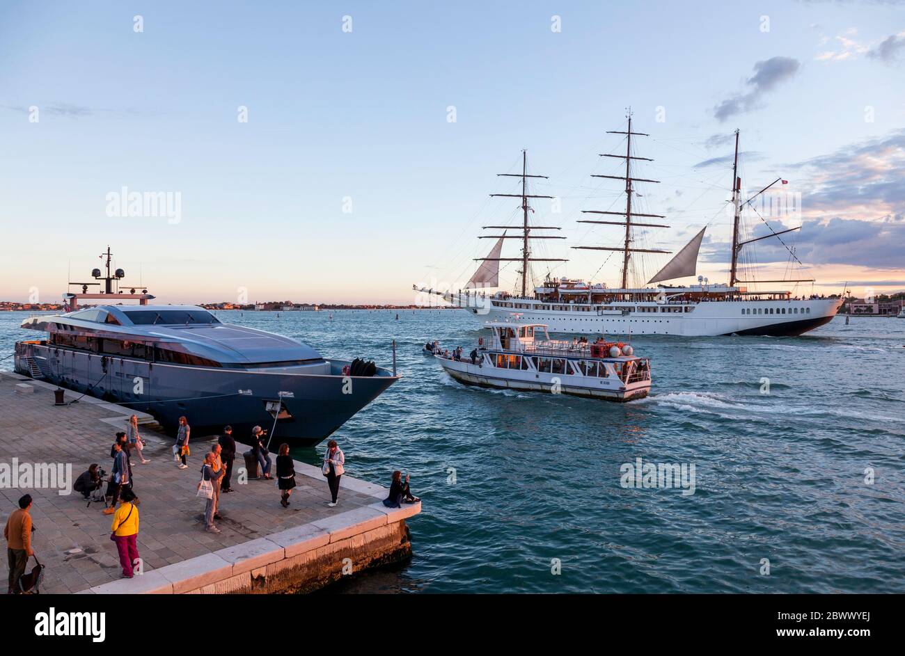 Trois voiliers à voile à mâts, MV Sea Cloud ll, laissant Venise sous un coucher de soleil chaud avec, en revanche, un bateau-bus et un yacht super au premier plan Banque D'Images