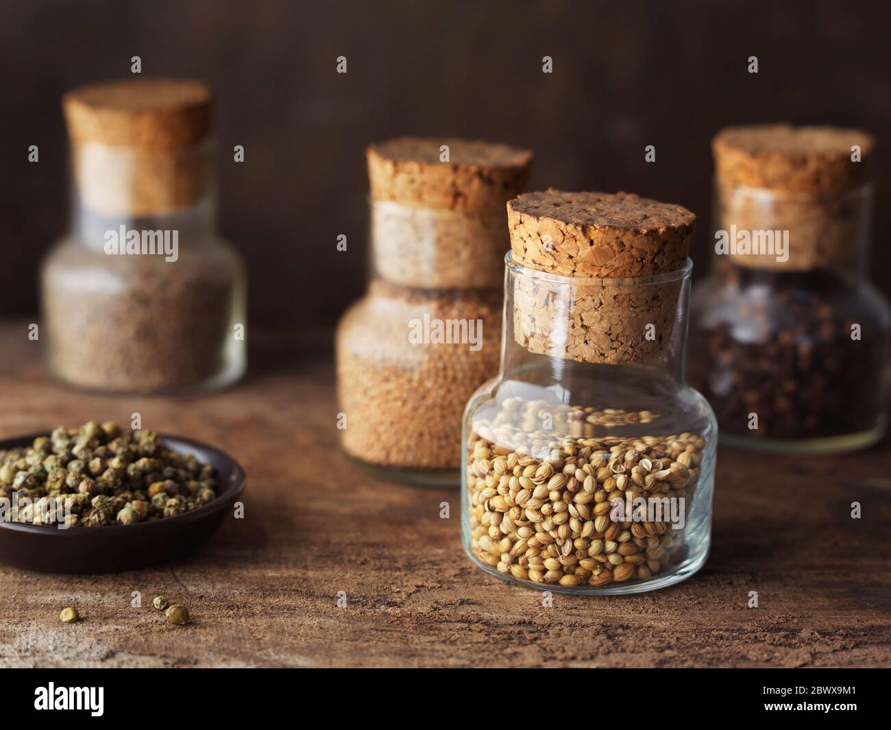 Pots d'épices (graines de coriandre, clous de girofle, graines de moutarde et graines de cumin) et grains de poivre vert dans un petit plat sur table en bois. Banque D'Images