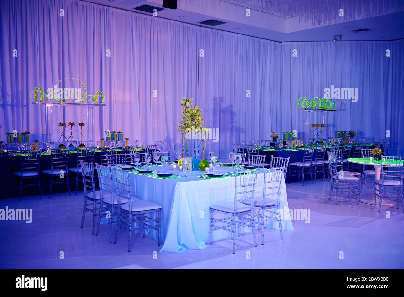 Table carrée élégante pour un mariage ou un événement social dans la salle de bal, orchidée et chaises en lucite, murs drapés Banque D'Images