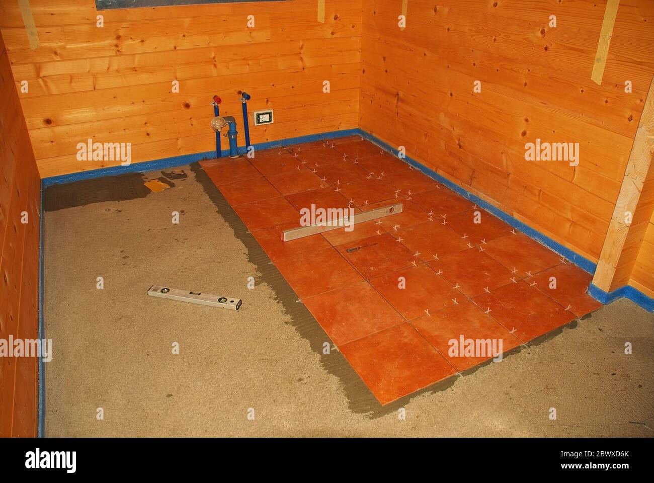 Plancher en béton dans une nouvelle maison en bois (sapin). L'adhésif pour carrelage a été appliqué et les carreaux de sol ont été posés. La mousse bleue protège les murs en bois Banque D'Images