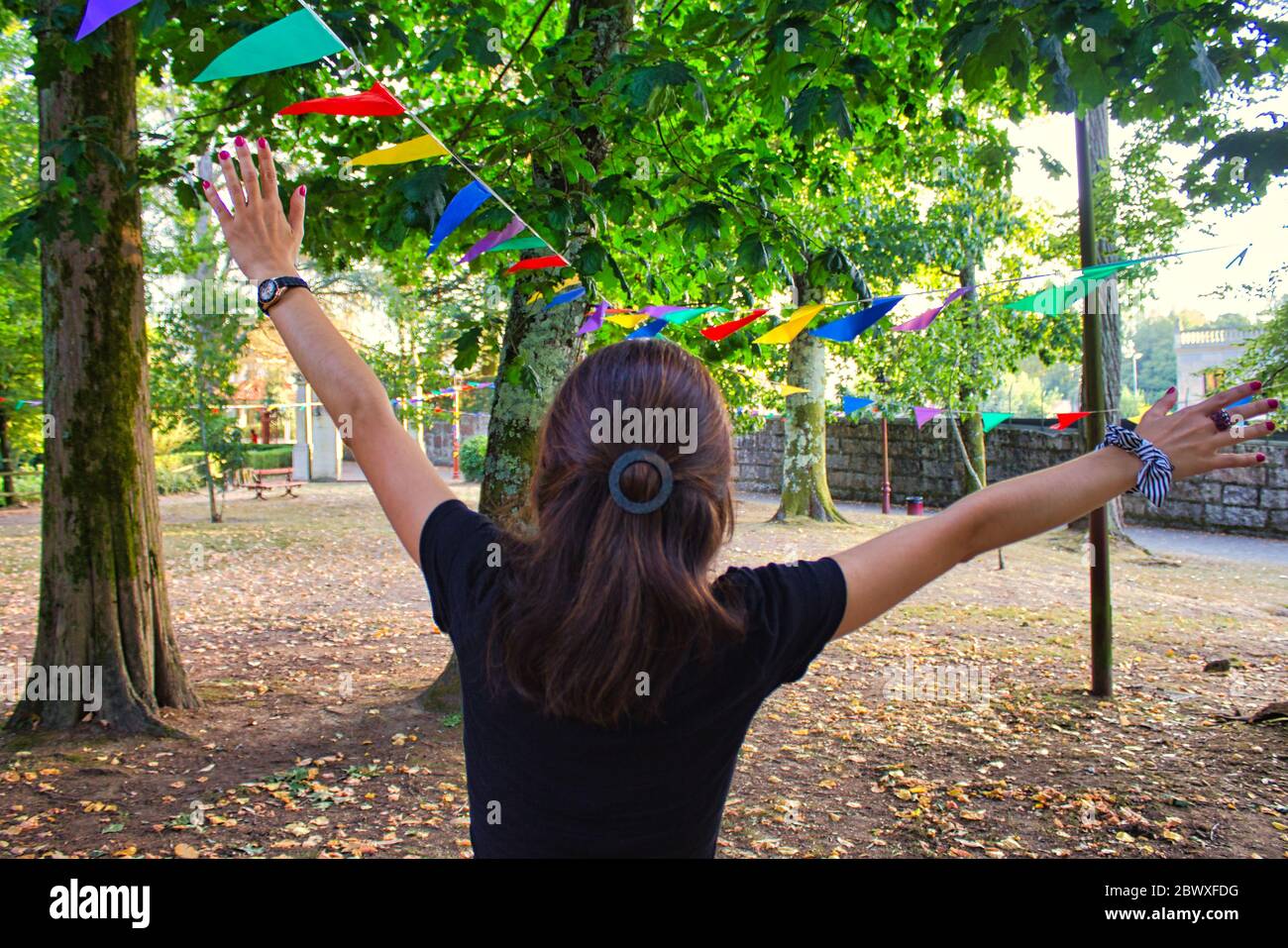 Jeune femme aux bras en haut avoir du plaisir dans un jour de festival dans un parc avec des drapeaux de décoration de différentes couleurs Banque D'Images