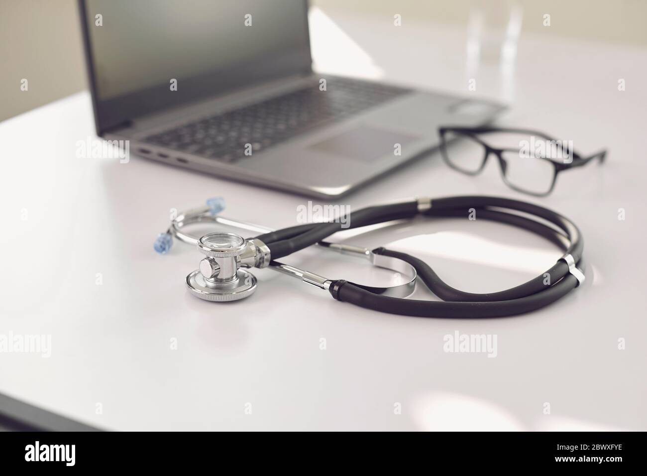 Médecin en ligne. Un stéthoscope est sur une table blanche avec un ordinateur portable en flou au bureau de l'hôpital. Banque D'Images