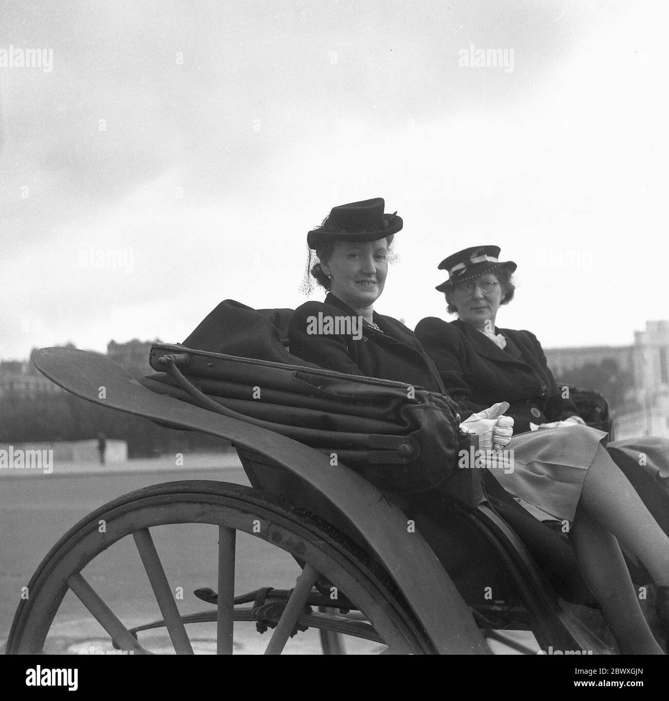 Années 1960, historique, deux femmes bien habillées qui se sont mises à la  porte pour une fonction, assises sur le siège d'une ancienne cabine ou  d'une poussette à roulettes en bois à