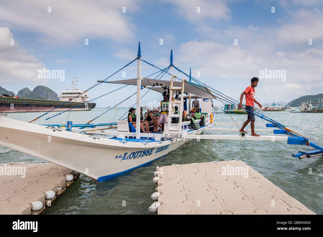 Un bateau à longue queue de pêcheur se charge de fournitures et de touristes pour partir en excursion d'une journée avec un énorme pétrolier derrière à l'île El Nido Philippines. Banque D'Images