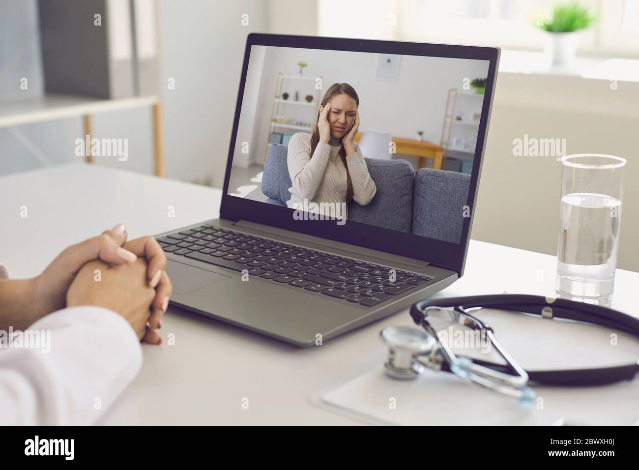 Médecin et patient en ligne. Le médecin a un ordinateur portable de consultation chat vidéo à l'écoute d'un patient avec un mal de tête dans le bureau de l'hôpital. Banque D'Images