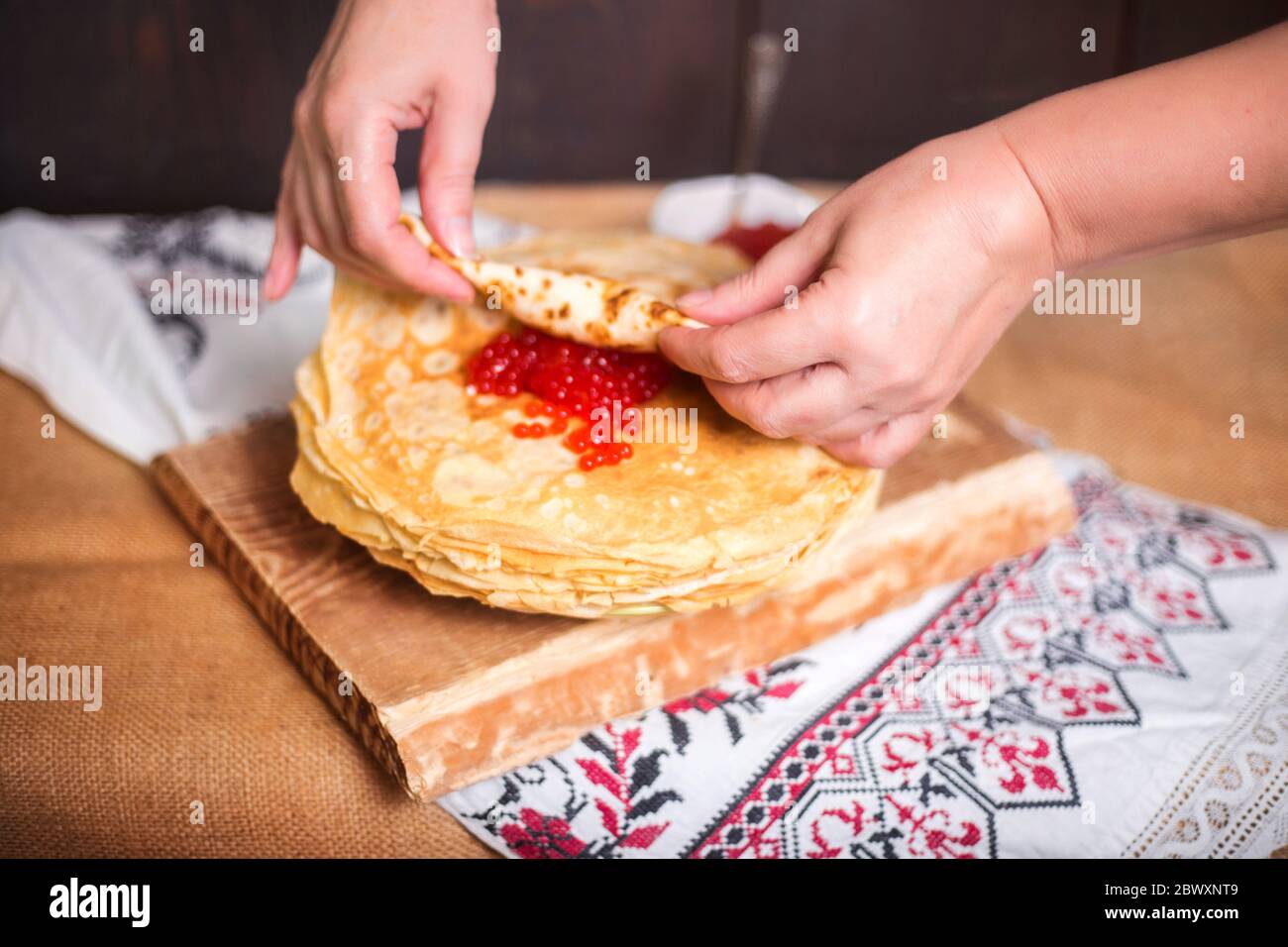 Une femme enveloppe le caviar rouge dans une crêpe chaude dans la cuisine, les mains se ferment. Banque D'Images