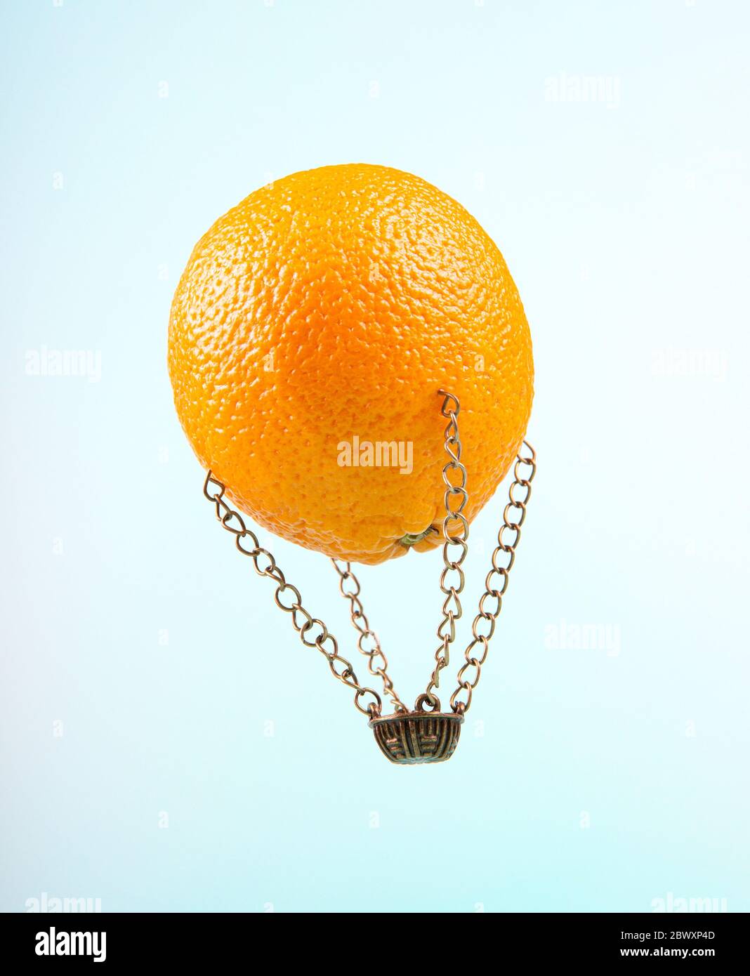 Ballon d'air chaud fait d'un orange et d'un petit panier en acier sur un fond bleu clair. Liberté d'été et excitation concept. Banque D'Images