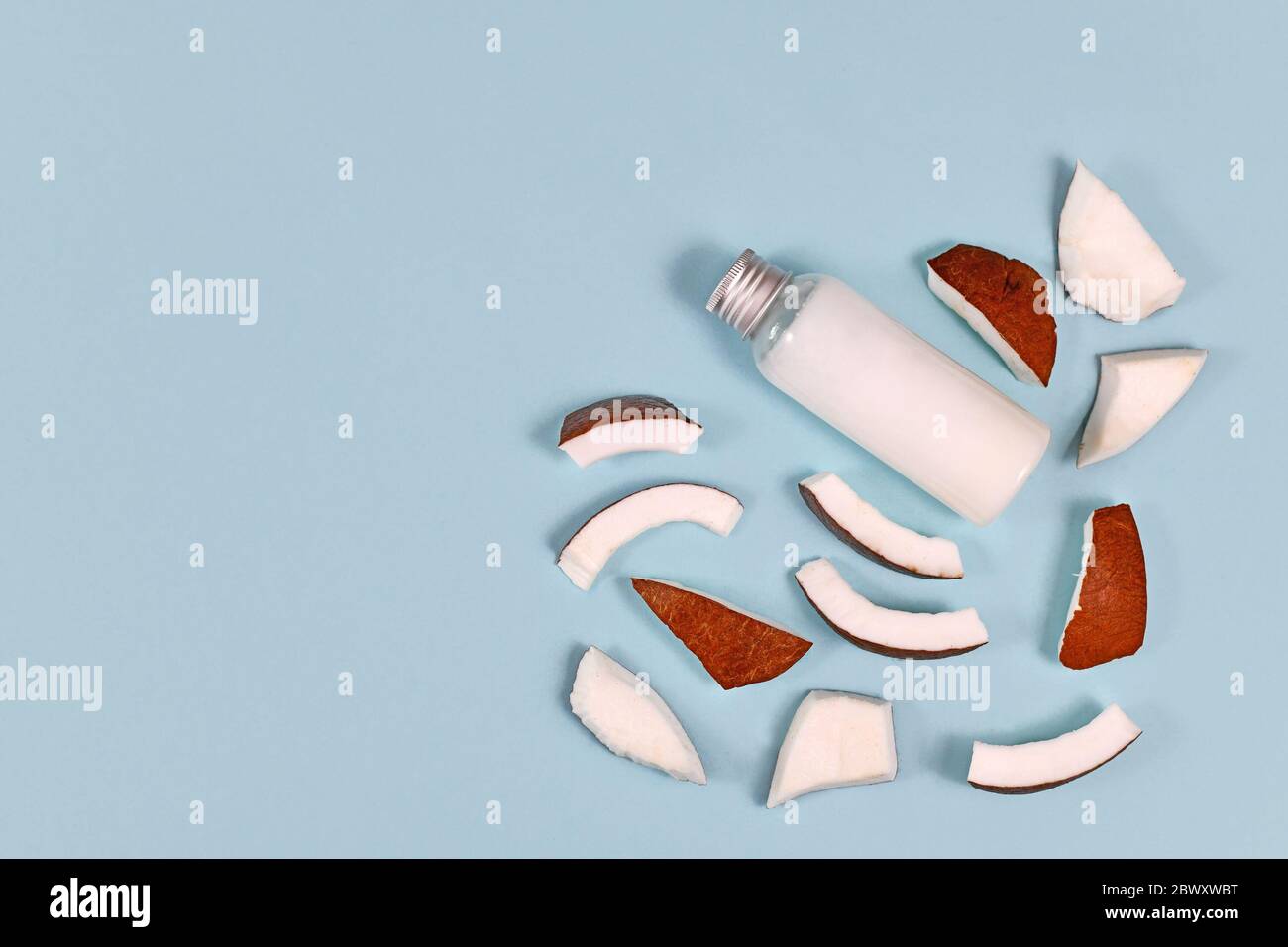 Tranches de fruits à la noix de coco et bouteille remplies d'huile de coco utilisées pour la préparation alimentaire et les produits cosmétiques de beauté sur fond bleu avec espace de copie Banque D'Images
