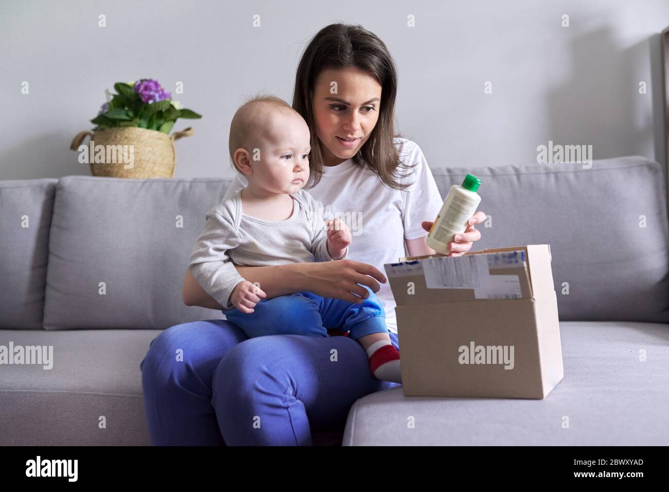 Jeune mère avec bébé dans ses bras déballant colis avec le shopping en ligne Banque D'Images