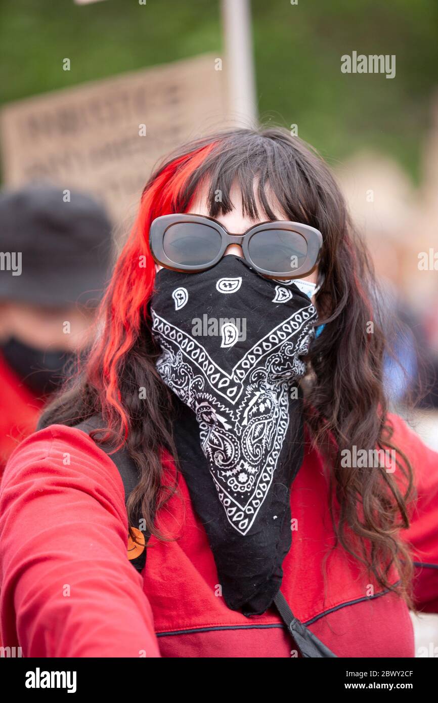 Femme avec une traînée rouge dans ses cheveux et portant des lunettes de soleil et une écharpe protectrice couvrant son visage, Londres, Angleterre, Royaume-Uni Banque D'Images