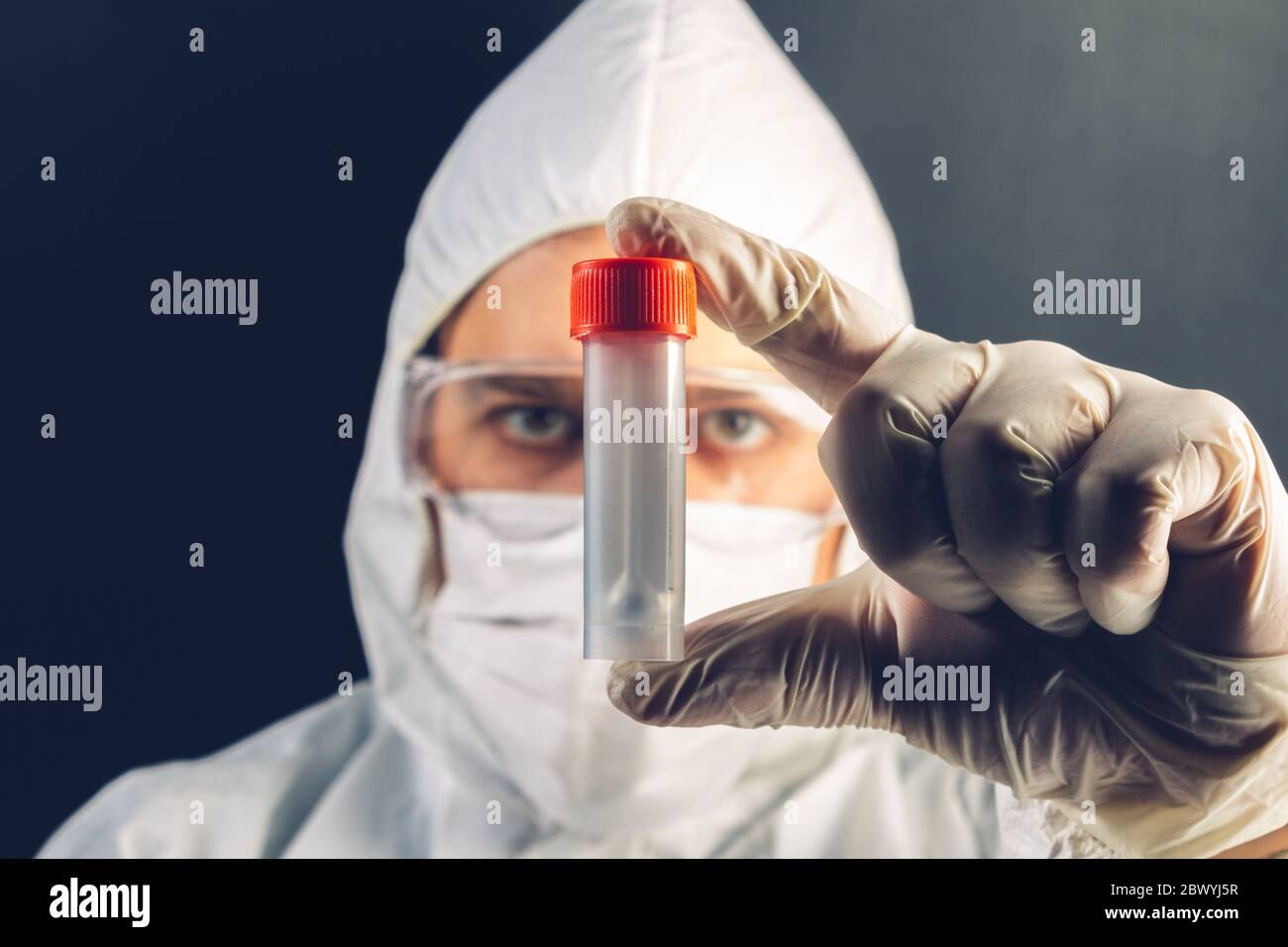 Photo d'un médic dans un masque, des gants et un costume de protection tenant un tube à essai. Banque D'Images