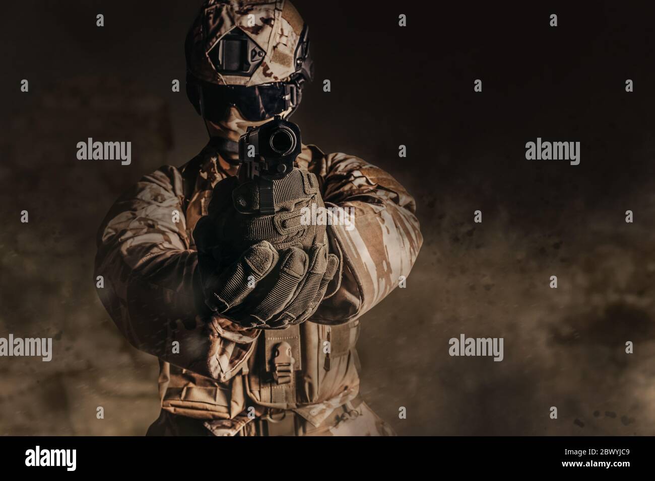Photo d'un soldat entièrement équipé en armure, casque, gants et lunettes pistolet visant à poser sur le fond du désert dusistant. Banque D'Images