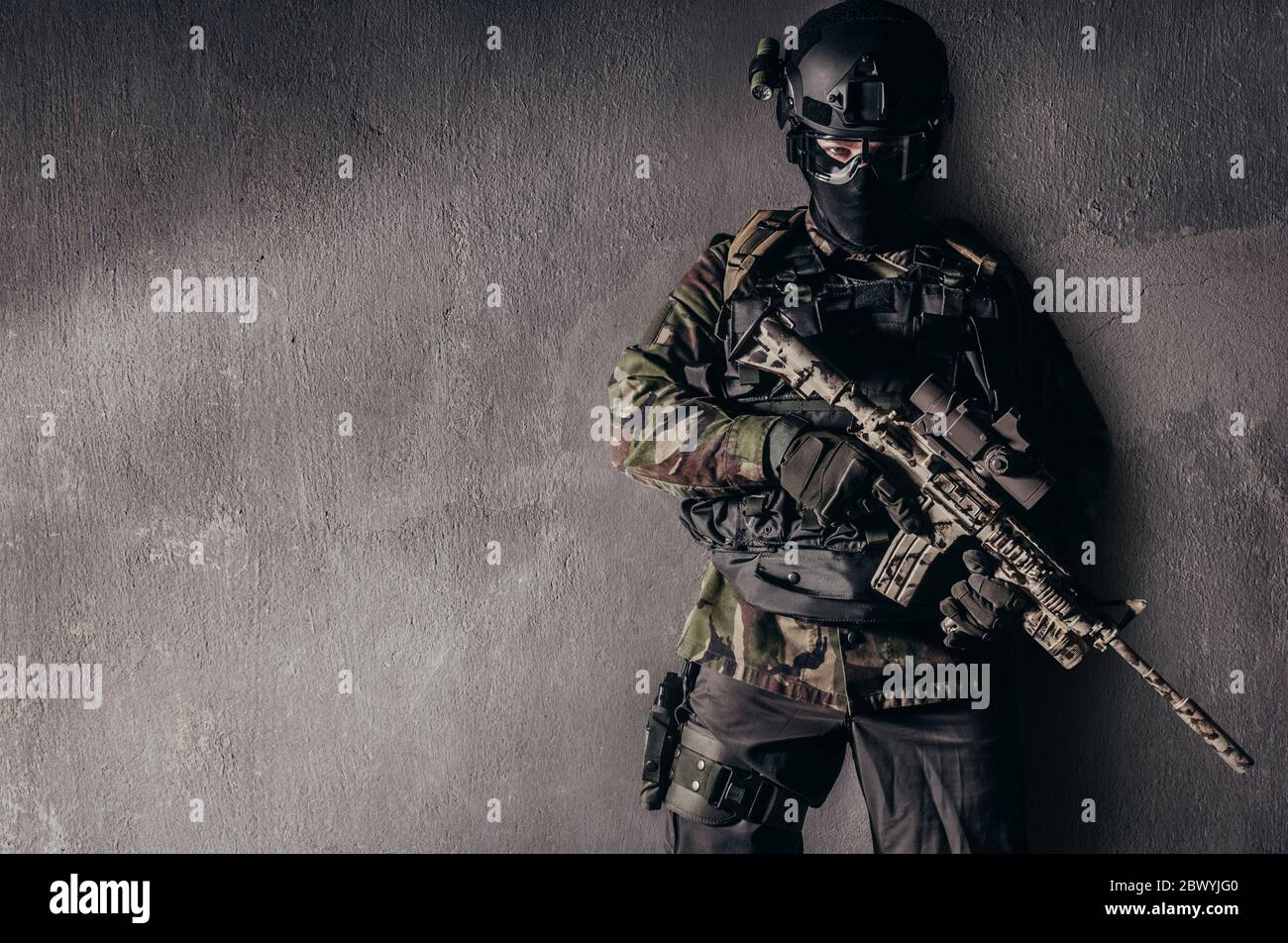 Photo d'un soldat entièrement équipé en uniforme de camouflage debout sur fond de mur en béton. Banque D'Images