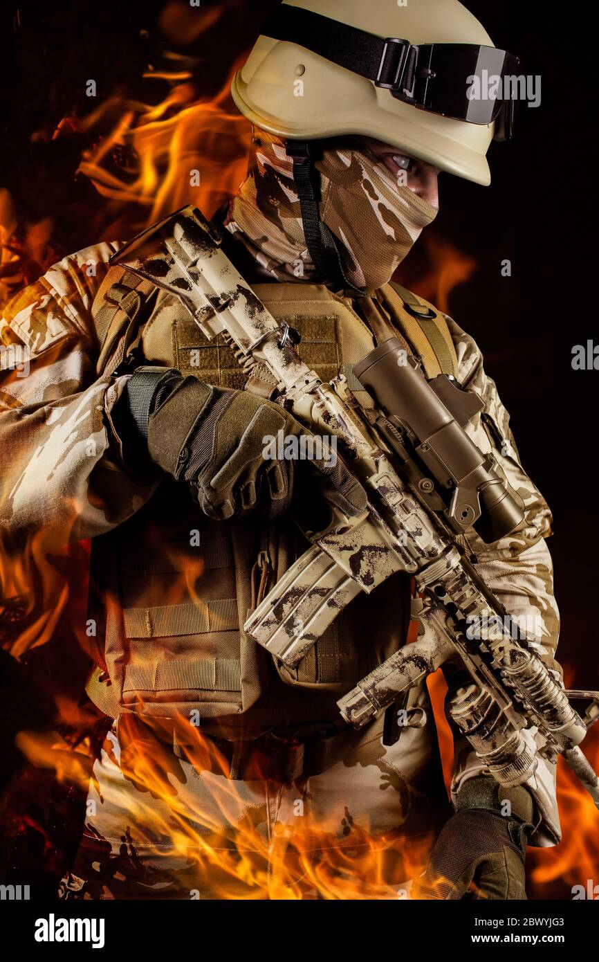 Photo d'un soldat entièrement équipé en uniforme de camouflage, casque, gants et armure tenant le fusil sur fond de feu de propagation. Banque D'Images