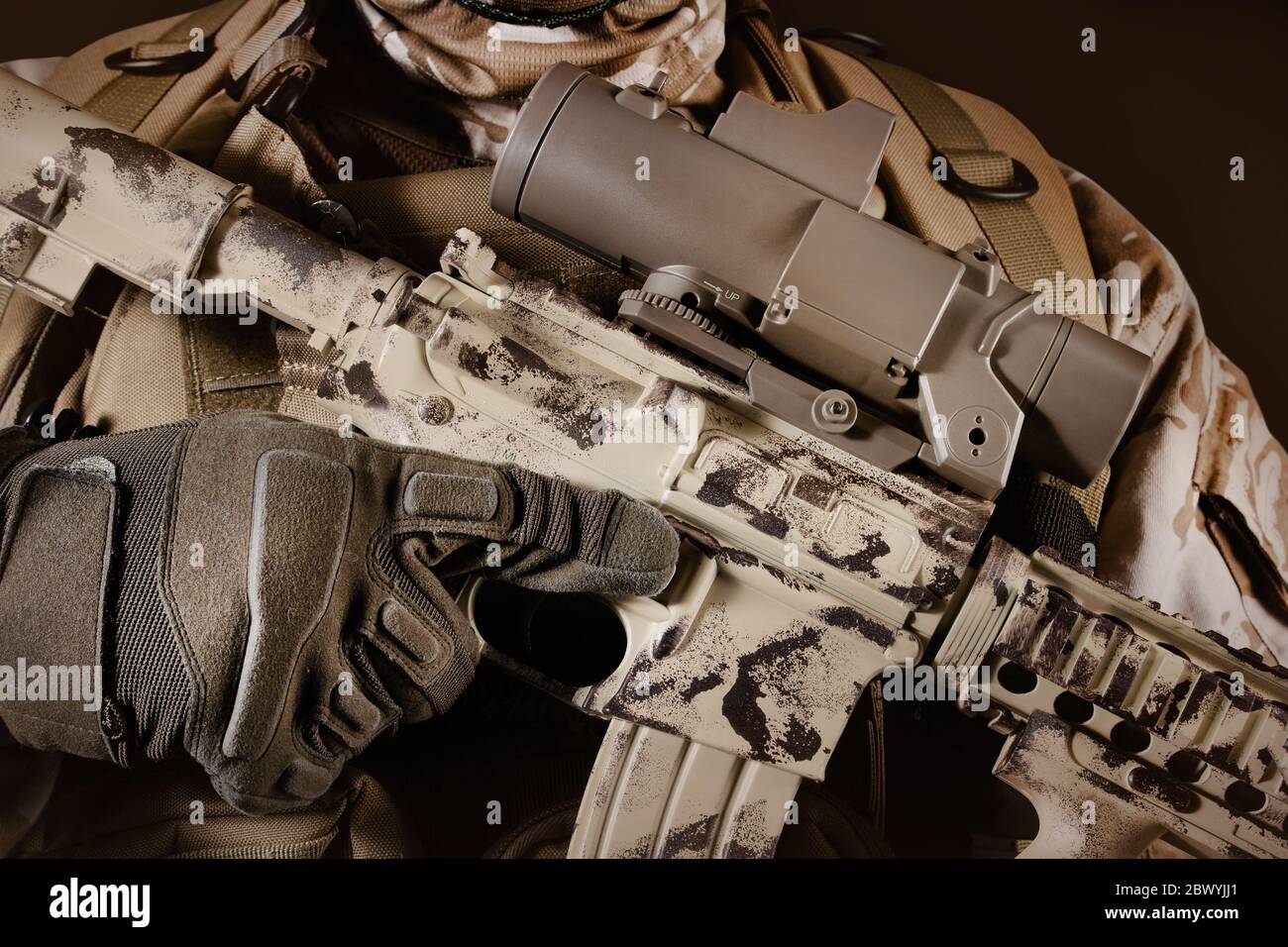 Photo d'un soldat du désert entièrement équipé tenant une carabine automatique avec clip sur fond marron foncé. Banque D'Images