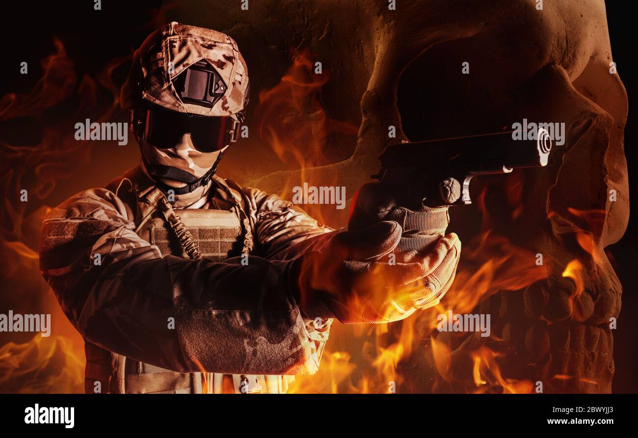 Photo d'un soldat entièrement équipé en armure, casque, gants et lunettes pistolet visant à poser sur le fond de crâne brûlant. Banque D'Images
