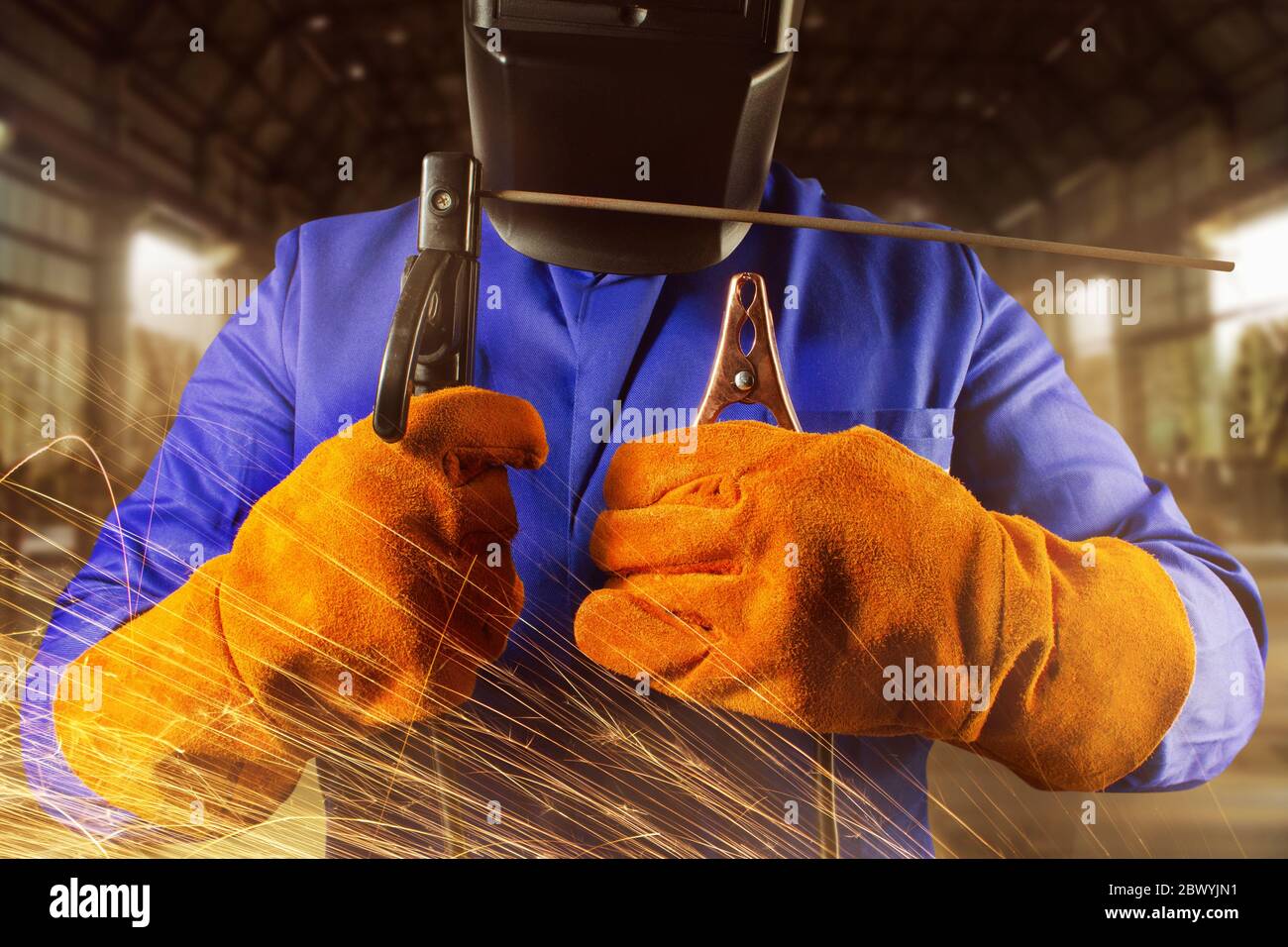 Photo d'un soudeur en uniforme, casque et gants tenant l'électrode et le  support de masse sur un fond industriel avec des étincelles Photo Stock -  Alamy