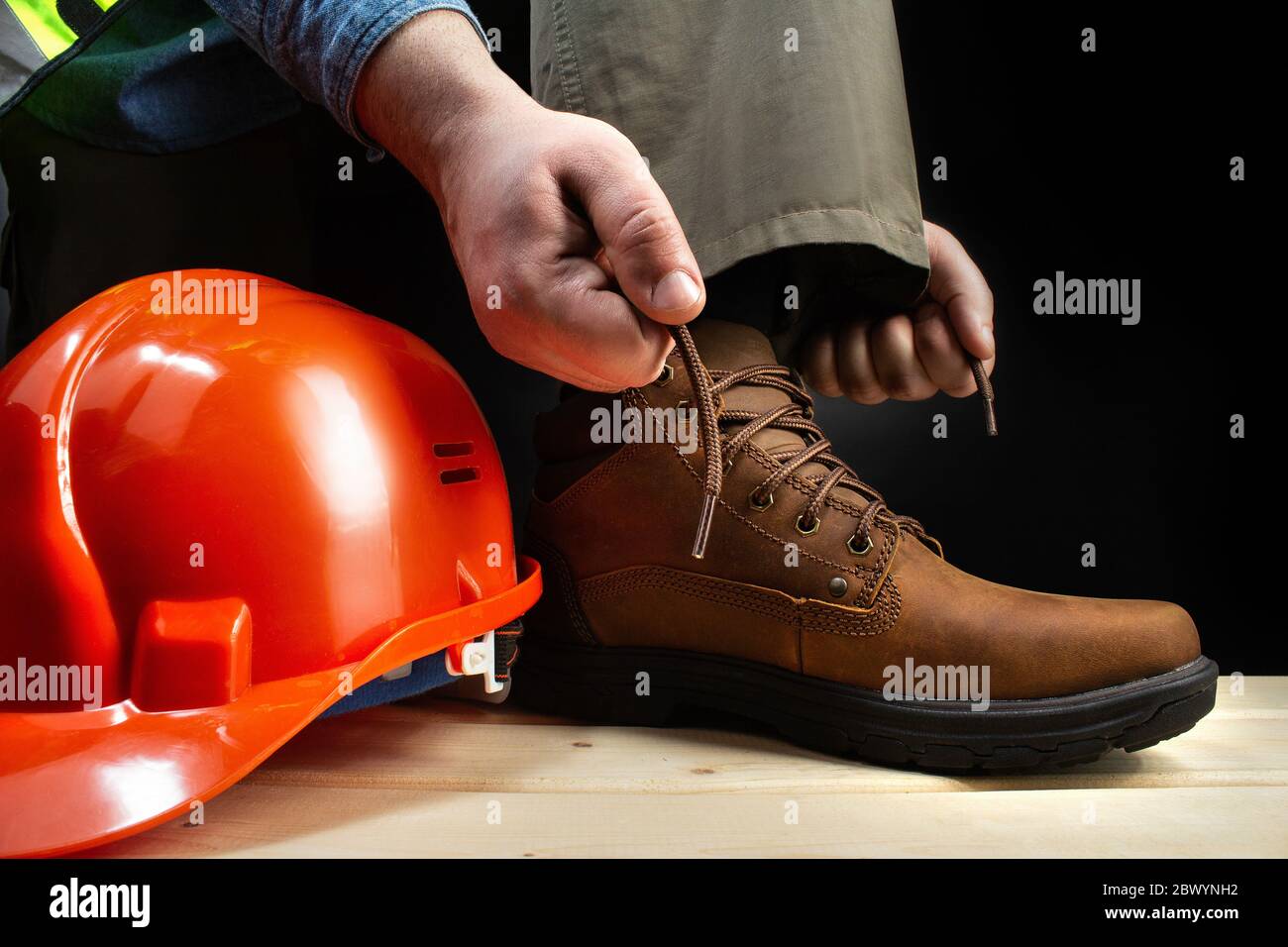 Photo d'un travailleur laçant une chaussure en cuir sur une surface avec un casque de protection. Banque D'Images
