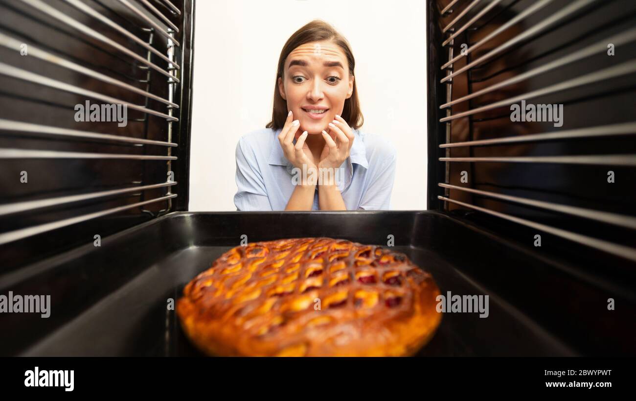 Une fille affamée a hâte de déguster une tarte maison savoureuse, vue depuis l'intérieur du four Banque D'Images