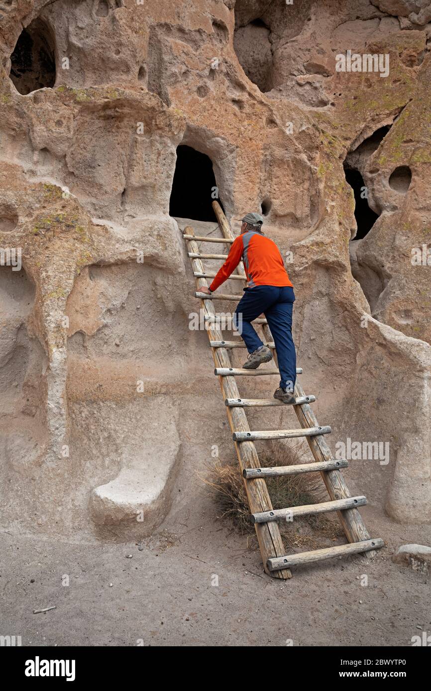 NM00454-00...NOUVEAU MEXIQUE - Visiteur grimpant en échelle de bois de style traditionnel jusqu'à une demeure ancestrale de la falaise de Pueblo au monument national de Bandelier. Banque D'Images