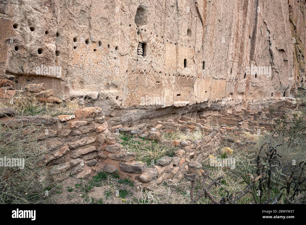 NM00465-00...NOUVEAU-MEXIQUE - fondations anciennes à la base d'une falaise avec des trous forés dans la pierre pour soutenir les toits et les planchers de la maison longue. Banque D'Images