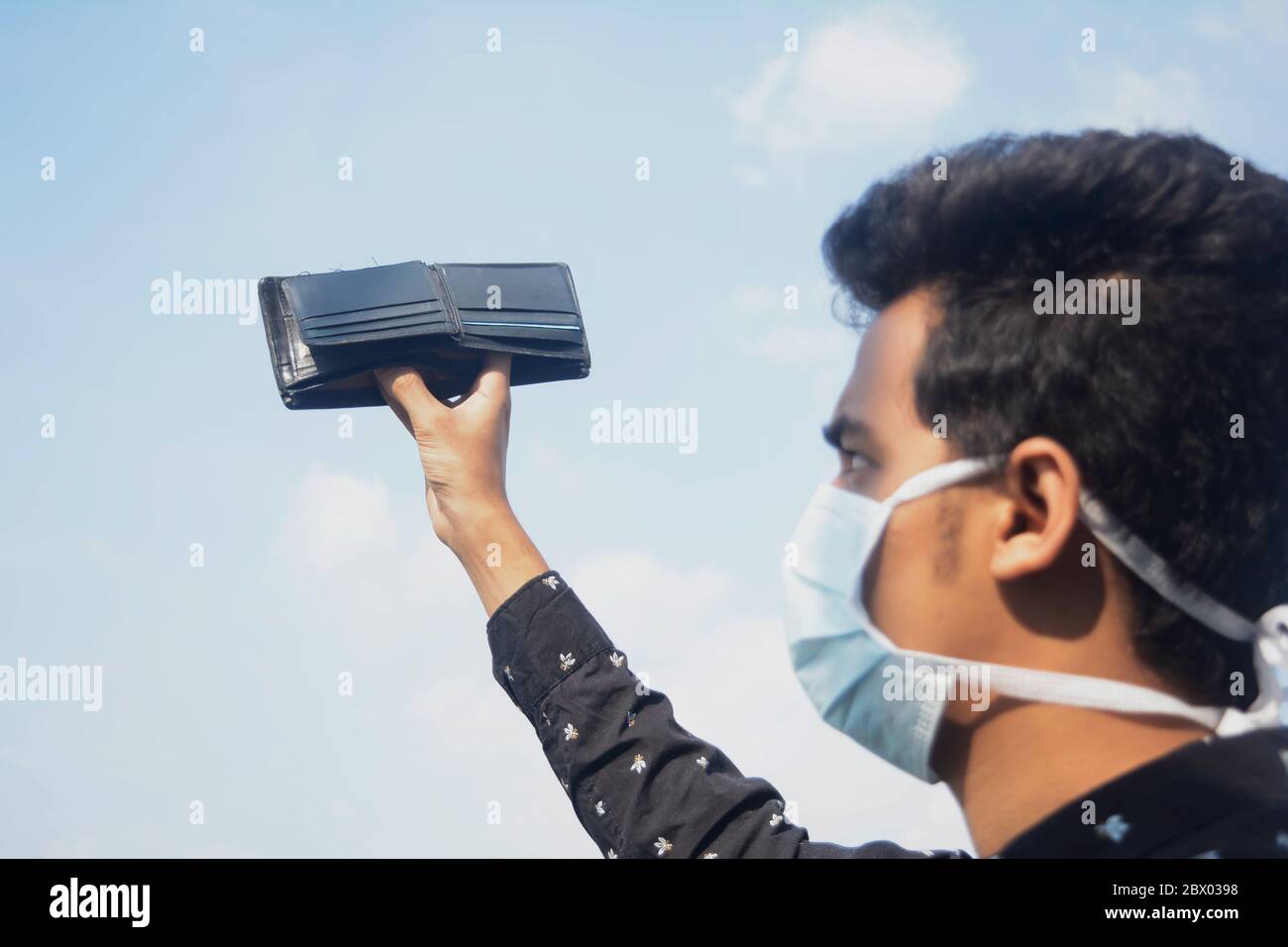 Jeune homme portant un masque facial de protection et montrant son portefeuille vide sur le nuage et le ciel background.selective se concentre sur le portefeuille. Banque D'Images